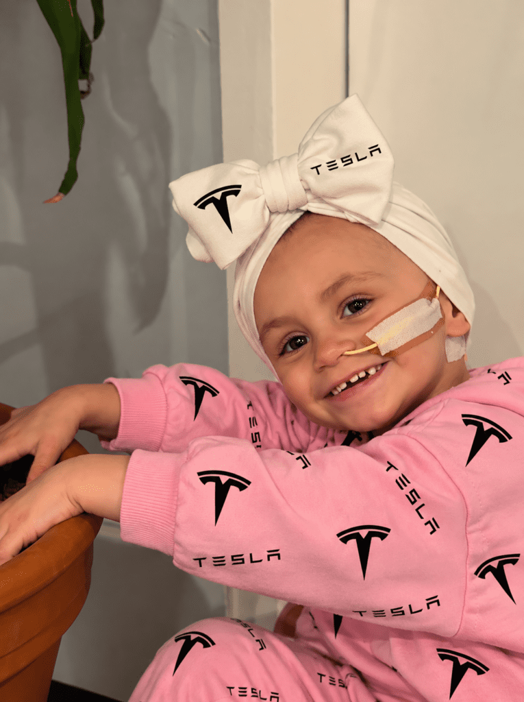 A smiling young cancer fighter in a white Tesla bow and pink Tesla outfit