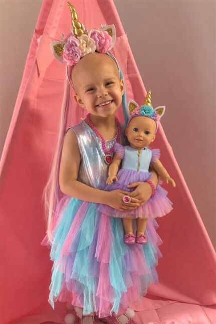 Smiling girl in a unicorn flower crown holding her 18-inch doll, both wearing matching Uni-Port dresses